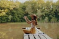 A woman yogi sits with her back to the riverbank on a bridge and meditates on relaxing her body in nature