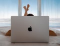 Womanl lying in bed using behind mackbook pro, panoramic windows, sea background