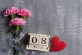 Womans day concept. Pink carnation flower with March 8 text on wooden block calendar and red heart and on gray wooden background