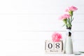 Womans day concept. Pink carnation flower in vase and red heart with March 8 text on wooden block calendar on white wooden Royalty Free Stock Photo
