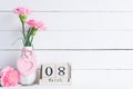 Womans day concept. Pink carnation flower in vase and red heart with March 8 text on wooden block calendar on white wooden Royalty Free Stock Photo