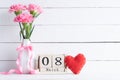 Womans day concept. Pink carnation flower in vase and red heart with March 8 text on wooden block calendar on white wooden Royalty Free Stock Photo