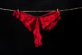 Womans erotic red underwear panties hanging on rope isolated on black background. Lace lingerie, woman sexy underwear. Royalty Free Stock Photo