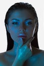Womans face bathed in blue light, her skin adorned with sparkling glitter, exudes a contemplative look
