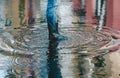 Womans feet with black rubber boots and blue jeans standing in a puddle of water after rain on a city street. Side view