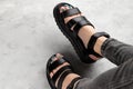 Womans feet with pedicure in black trendy sandals on gray background Royalty Free Stock Photo