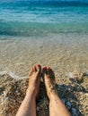 Womans feet with red nails pedicure and sand on golden sandy beach in blue turquoise sea waters. Holiday concept near Royalty Free Stock Photo