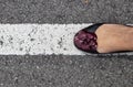 Womans foot in flat back shoe with purple flower on white stripe on asphalt - walking the line Royalty Free Stock Photo