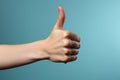 Womans hand gestures a thumbs up against serene pastel blue backdrop
