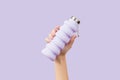 Womans hand holding collapsible reusable lilac water bottle on purple background. Zero waste