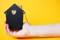 womans hand holding little toy house made of chalk board on a orange background. Royalty Free Stock Photo