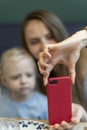 Womans hand holds phone against the blurry background of mother and daughter. Woman with child takes selfie on smartphone