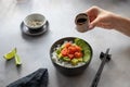 Womans hand holds a sauceboat with soy sauce over a dark bowl with salmon, rice, avocado and cucumber Royalty Free Stock Photo