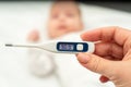 A womans hand holds a thermometer showing the temperature on the background of a blurred baby lying on the bed Royalty Free Stock Photo