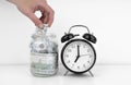 Womans hand put dollar bancnote into a glass jar with alarm clock Royalty Free Stock Photo