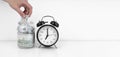Womans hand put dollar bancnote into a glass jar with alarm clock Royalty Free Stock Photo