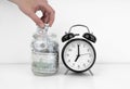 Womans hand put dollar bancnote into a glass jar with alarm clock Royalty Free Stock Photo