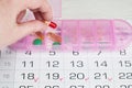 Womans hand puts a capsule in a pink plastic pill organizer