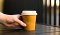 womans hand reaches for paper cup coffee with white lid. Table open veranda cafe Royalty Free Stock Photo