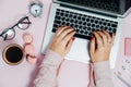 Womans hand writing on Laptop on pink plant macaroons alarm clock Top View Royalty Free Stock Photo