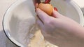 Womans hands broking yellow egg in bowl with ingredients for dough.