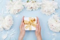 Womans hands giving gift or present box decorated white peony flowers on pastel table top view. Flat lay composition for birthday Royalty Free Stock Photo