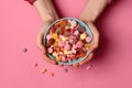 Womans Hands Holding Bowl Of Assorted Candies On Pink Background, Top View. Generative AI