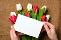 Womans hands holding a card with copy space for text above burlap canvas with tulips flowers. Greeting card for International Woma Royalty Free Stock Photo