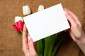 Womans hands holding a card with copy space for text above burlap canvas with tulips flowers. Greeting card for International Woma Royalty Free Stock Photo