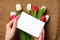 Womans hands holding a card with copy space for text above burlap canvas with tulips flowers. Greeting card for International Woma Royalty Free Stock Photo