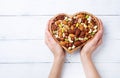 Womans hands holding heart shaped bowl with mixed nuts on white table top view. Healthy food and snack Royalty Free Stock Photo