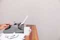 The womans hands typing on an old-fashioned typewriter. On the table are glasses and there is a mug. Neutral background