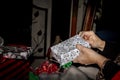 Womans hands unwrapping Christmas package with dark room and fireplace and pile of gifts in background - Selective focus