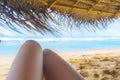 Womans legs under the sunshade on the sunny tropical beach Royalty Free Stock Photo