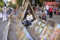 Women, artists, sitting on a pavement, their paintings placed on asphalt, blurred people on a background