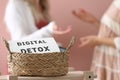 Women chatting against pink background, focus on wicker basket with sign DIGITAL DETOX