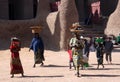 Women and children carry market goods on their heads, walking past the Great Mosque of Djenne, Mali