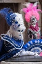 Two masks in costume with fans and ornate painted feathered masks at Venice Carnival.