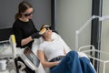 A woman on a couch in goggles undergoing a photorejuvenation procedure. Hardware cosmetology.