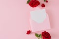 Flat lay photo of red roses with leaves and open envelope with white card on pastel pink background Royalty Free Stock Photo