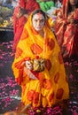 women devotee standing in river and praying with religious offerings for sun god in Chhath festival