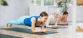 Women of different ages standing in Dolphin Plank Pose or Makara Adho Mukha asana during yoga training in gym studio