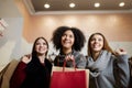 Women of diverse ethnicity with shopping bags posing in mall on sale. Portrait of three smiling multiracial girls look Royalty Free Stock Photo