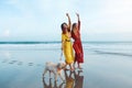 Women And Dog On Beach. Barefoot Girls With Pet On Dog-Friendly Coast. Happy Models Walk With Cute Puppy