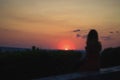 Women in dress sitting on stone on top of hill blurred defocused silhouette. She views red sun circle falling down Royalty Free Stock Photo