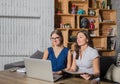 Two young woman managers watching webinar on laptop computer, sitting in modern interior.