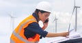 Women engineer using mobile phone and laptop for working on-site at wind turbine farm