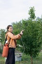 Women farmer spraying fertilizers and trace elements with portable sprayer on trees