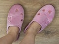 Women feet are shod in a home pink slippers. Cozy, warm and comfortable domestic shoes. On a brown wooden floor Royalty Free Stock Photo