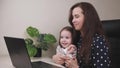 A woman freelancer with a small child in her arms is talking through a laptop monitor screen, work in a mother& x27;s home Royalty Free Stock Photo